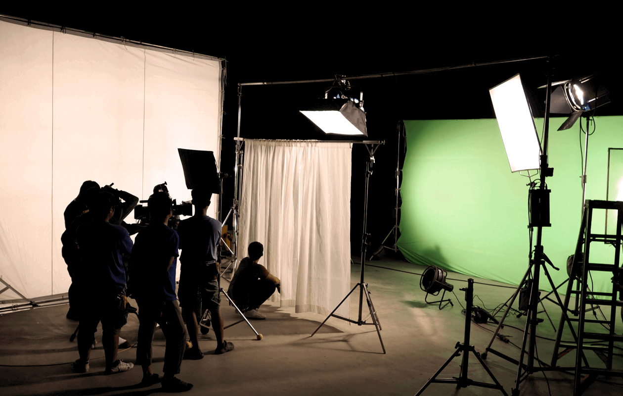 A video production set with a green screen, lighting and a camera crew. 